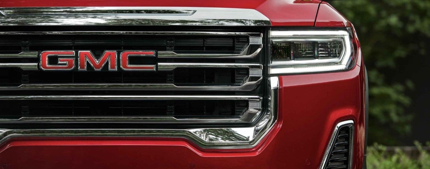 Grille and headlight of a red 2023 GMC Acadia SLT.